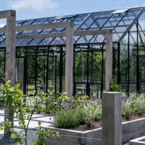 A glass greenhouse surrounded by greenery and garden beds.