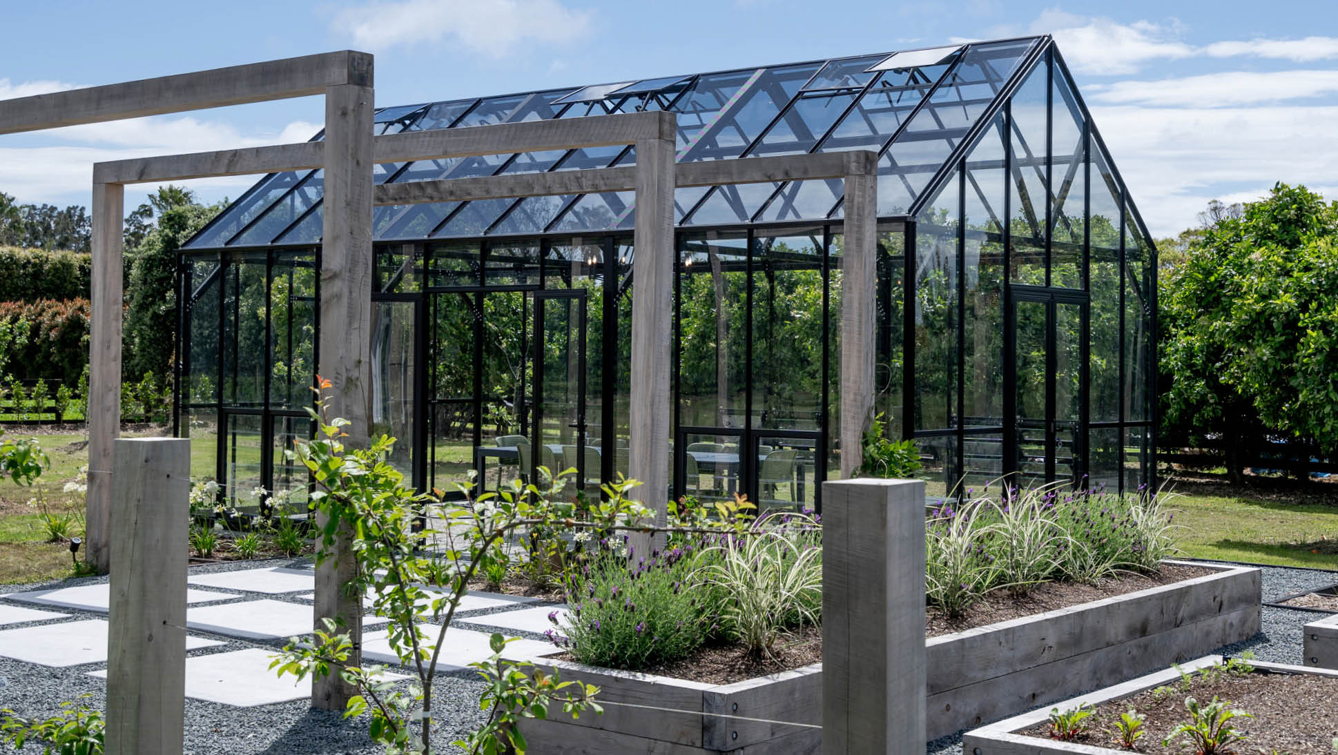 A glass greenhouse surrounded by greenery and garden beds.